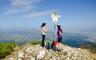 Hikers at a summit signpost in Piatra Craiului National Park, Brasov, with panoramic views.