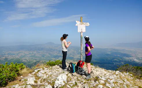 Hikers at a summit signpost in Piatra Craiului National Park, Brasov, with panoramic views.