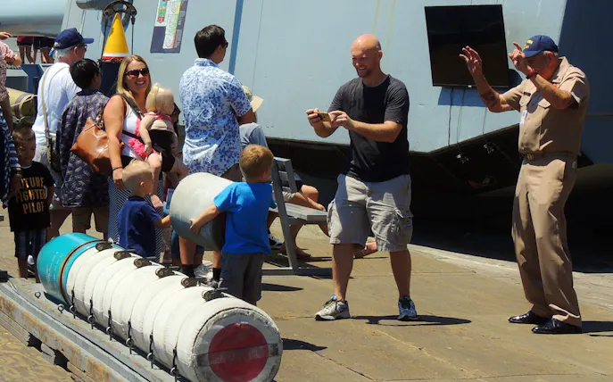 Visitors on a guided tour interact with a crew member on a museum ship deck.