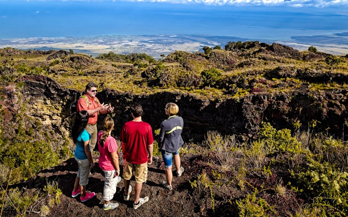 Guide showing visitors the edge of Hualalai volcano crater in Hawaii.