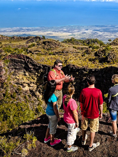 Guide showing visitors the edge of Hualalai volcano crater in Hawaii.