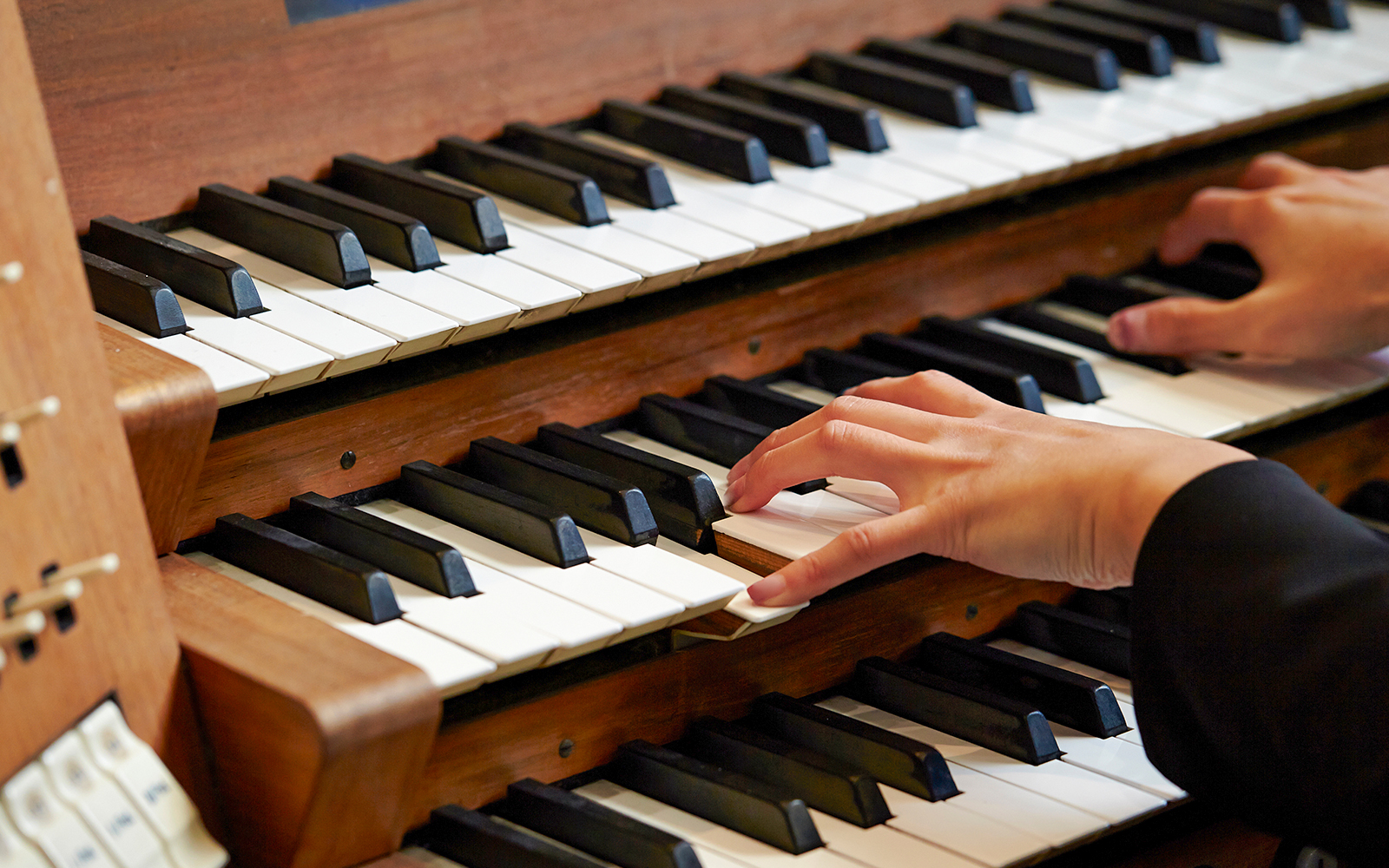 Hands playing a church organ keyboard.
