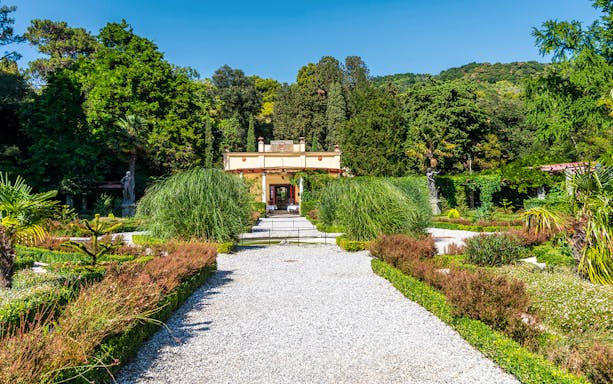 Miramare Castle garden path with lush greenery and statues, Trieste, Italy.