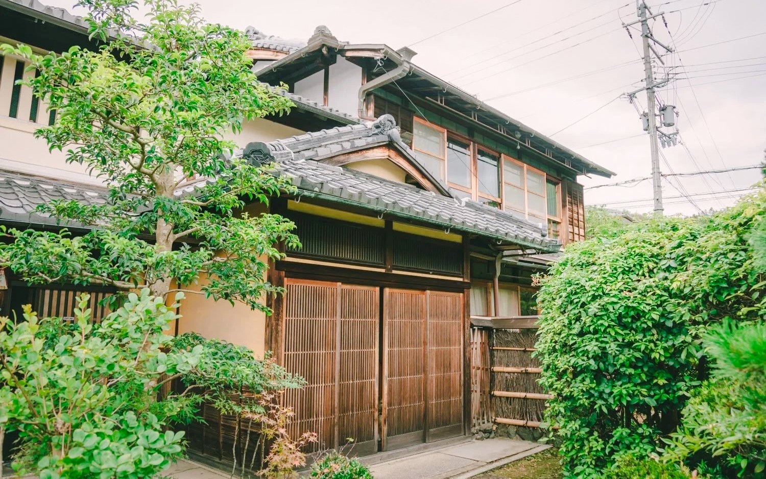 Traditional Japanese house with wooden sliding doors, surrounded by lush greenery, ideal for a tea ceremony experience.
