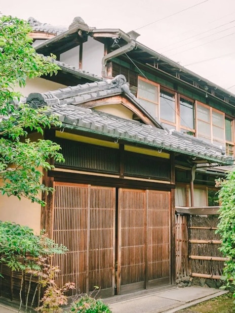Traditional Japanese house with wooden sliding doors, surrounded by lush greenery, ideal for a tea ceremony experience.