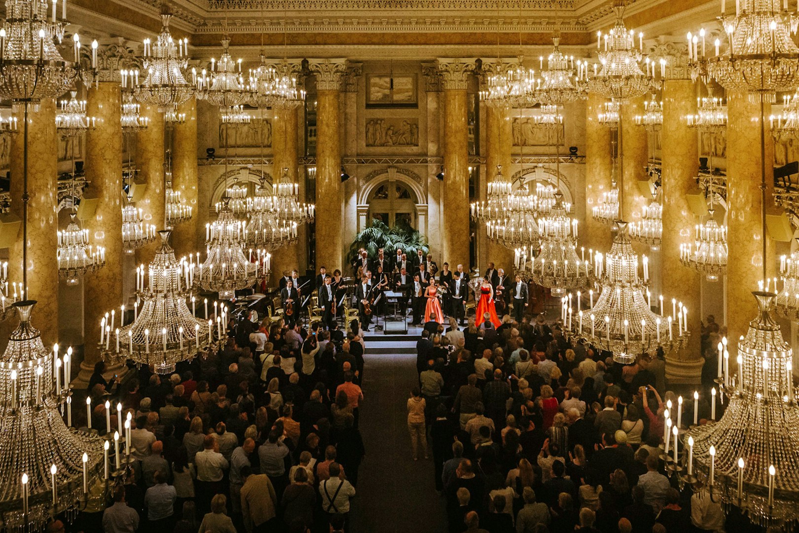 Vienna Hofburg Orchestra performing in a grand chandelier-lit hall.