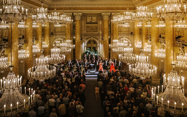 Vienna Hofburg Orchestra performing in a grand chandelier-lit hall.