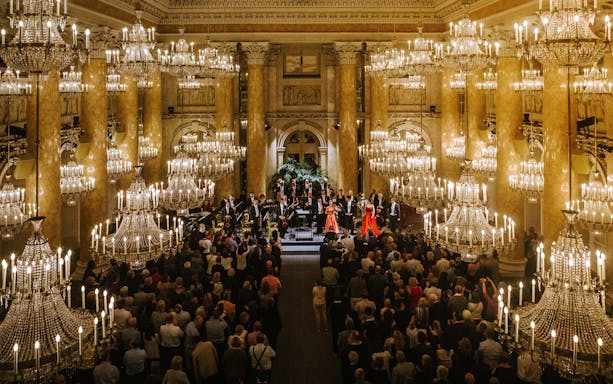 Vienna Hofburg Orchestra performing in a grand chandelier-lit hall.