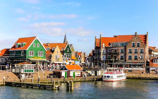 Dutch village waterfront with traditional houses and a tour boat docked.
