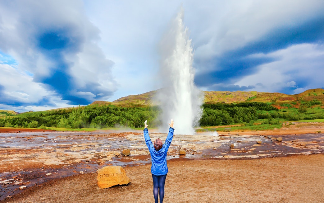 Woman raising arms near erupting Strokkur Geyser, Iceland.