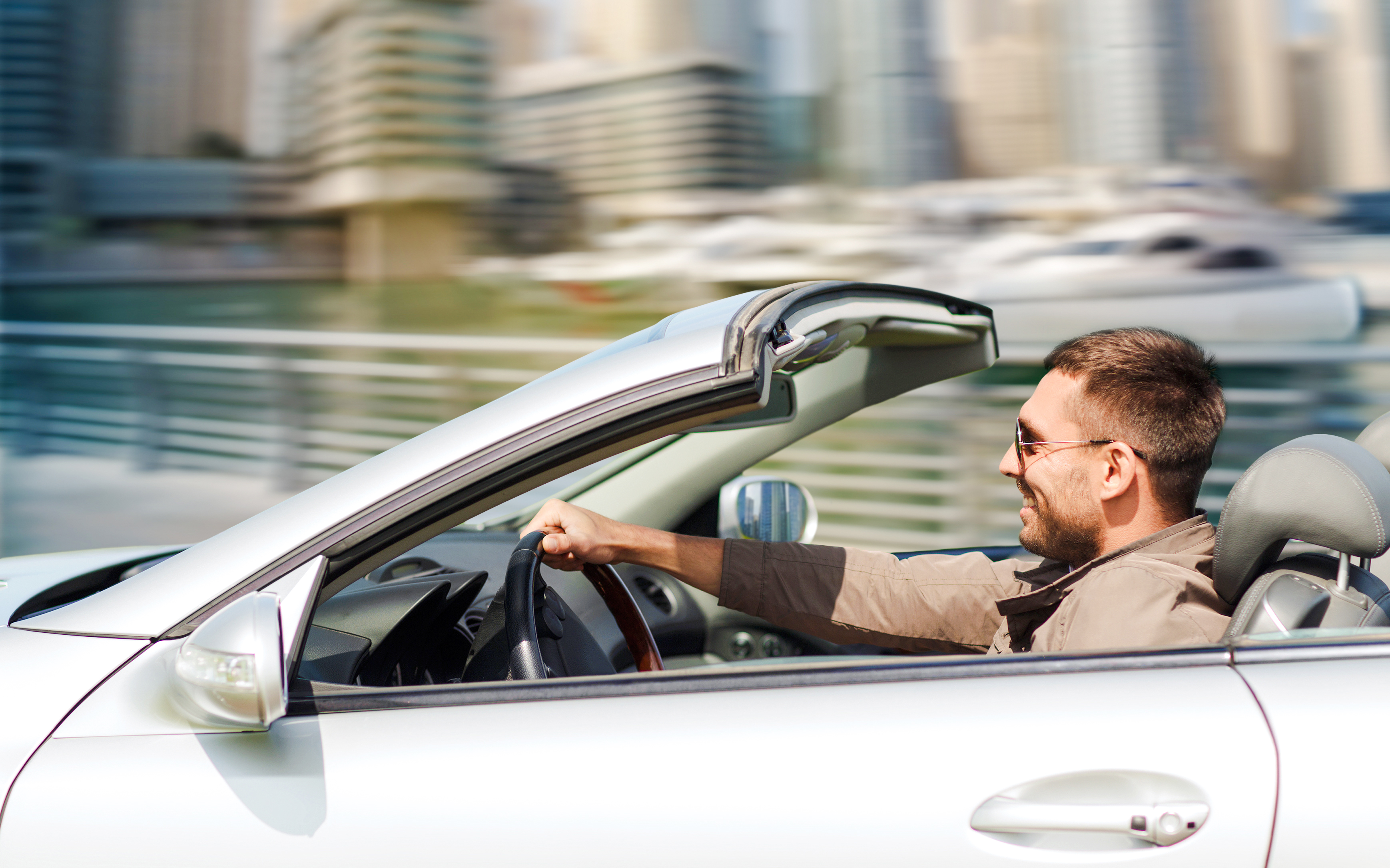 Man driving convertible in Dubai with city skyline in background.