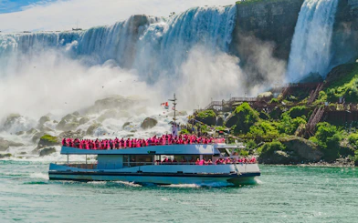 Boat cruise approaching Niagara Falls with passengers in pink raincoats.