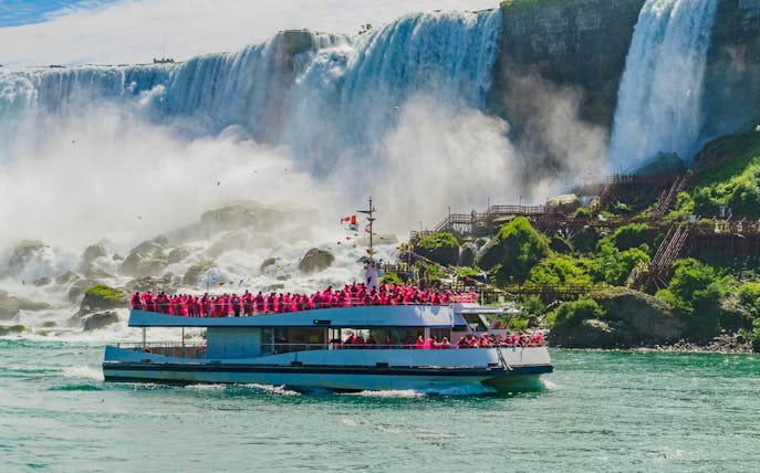 Boat cruise approaching Niagara Falls with passengers in pink raincoats.