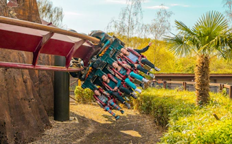 Roller coaster riders at Thorpe Park on an inverted track amidst greenery.