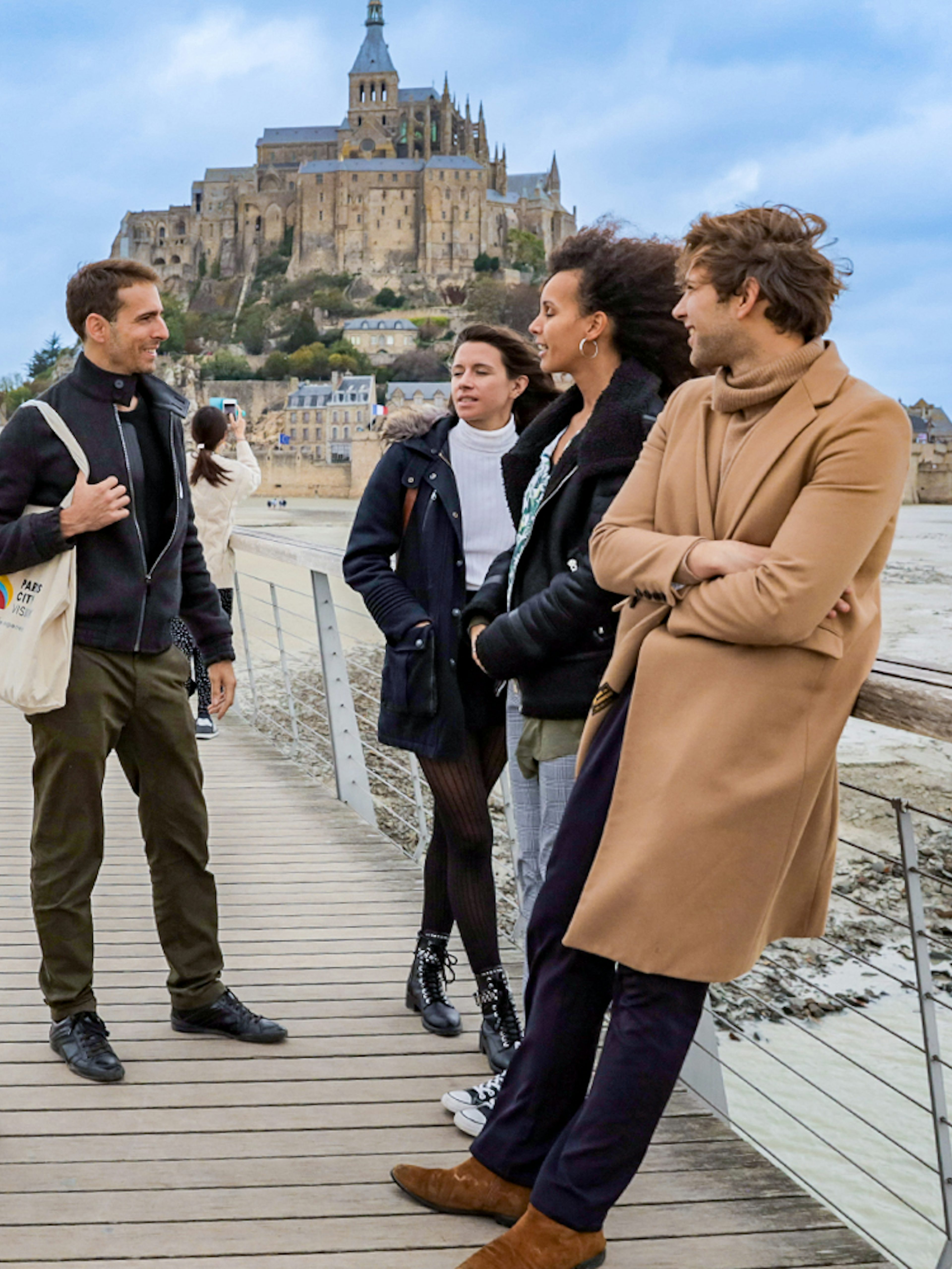 Group of tourists on a bridge with Mont Saint Michel in the background.