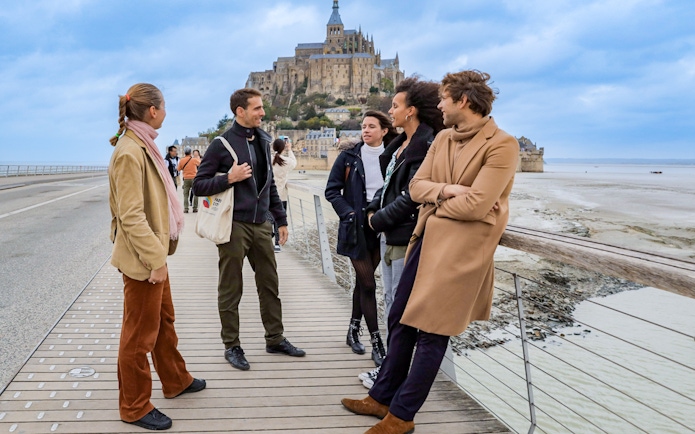 Group of tourists on a bridge with Mont Saint Michel in the background.