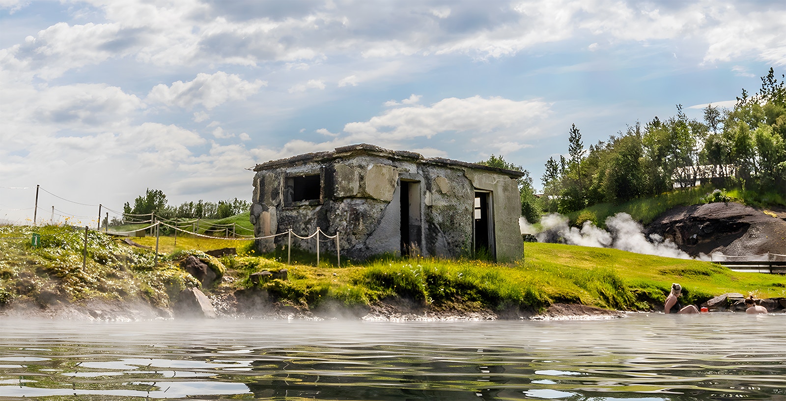 Old stone building by the Secret Lagoon with steam rising from hot springs, Iceland.
