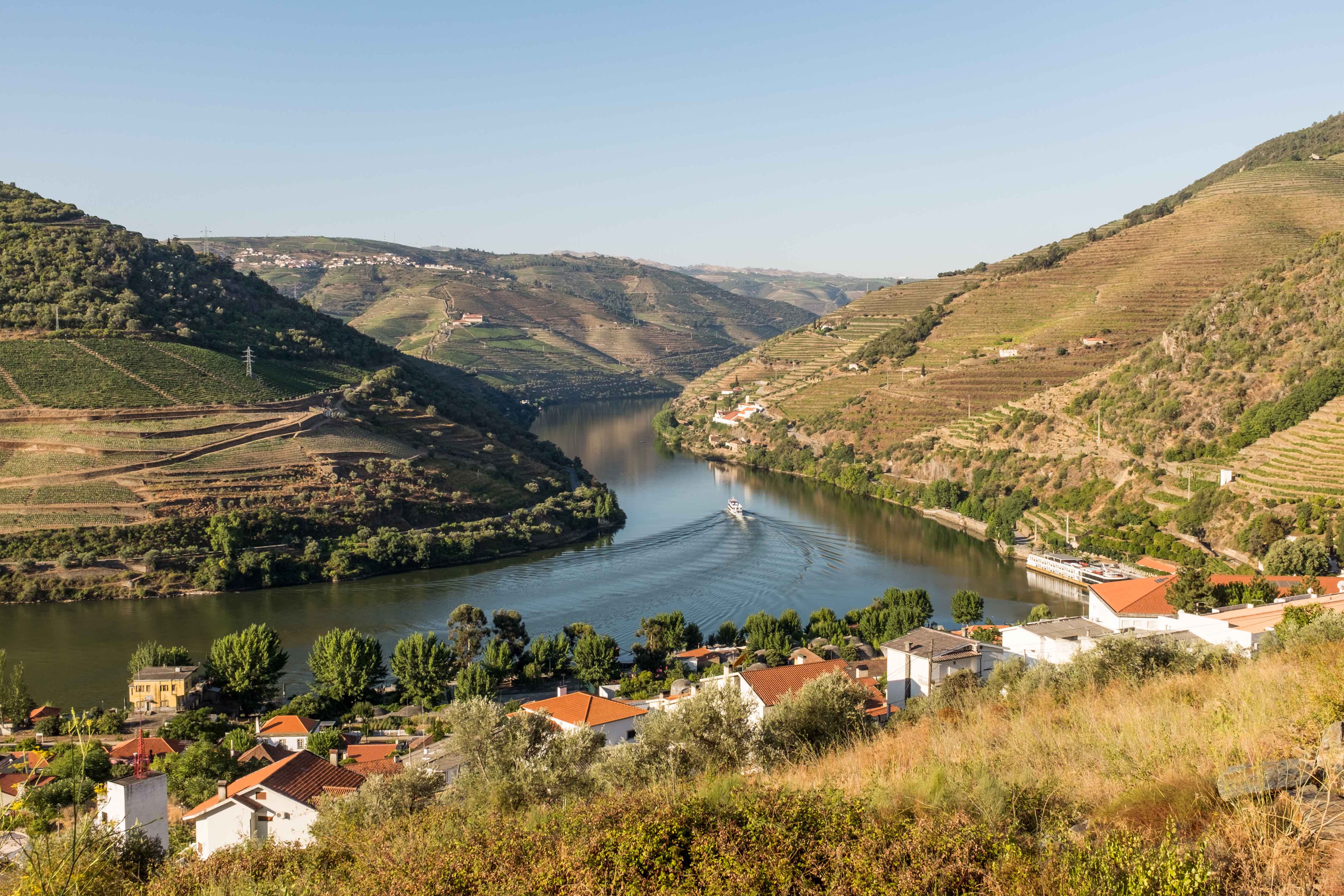 Vineyards and river in Douro Valley, Portugal, with a boat cruising through the scenic landscape.