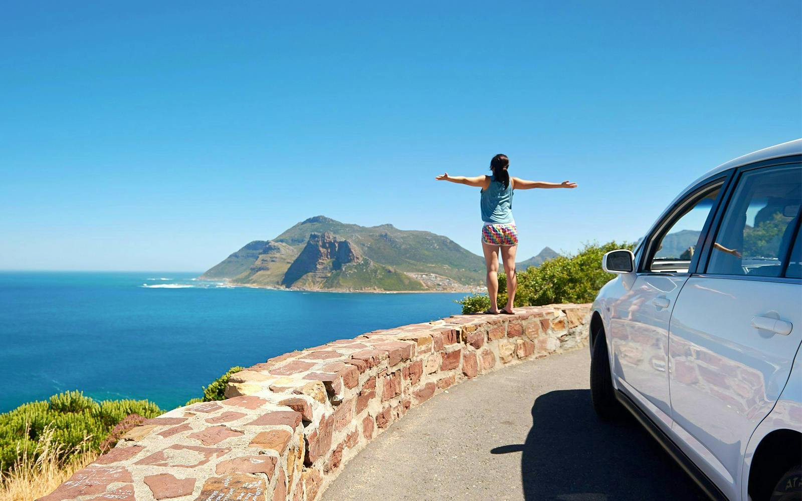 Person standing on Chapman's Peak Drive overlooking ocean and mountains in Cape Town, South Africa.