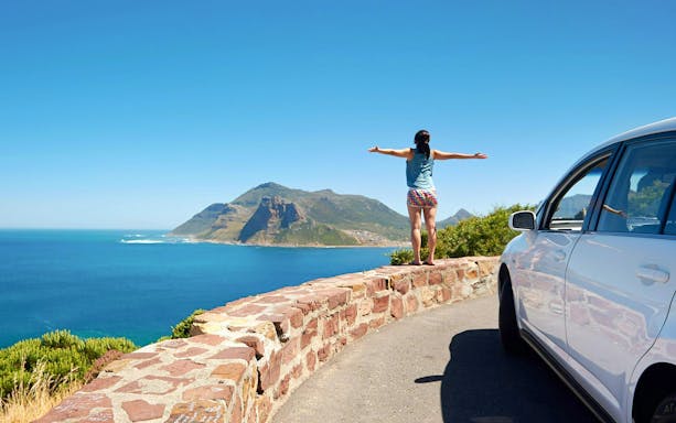 Person standing on Chapman's Peak Drive overlooking ocean and mountains in Cape Town, South Africa.