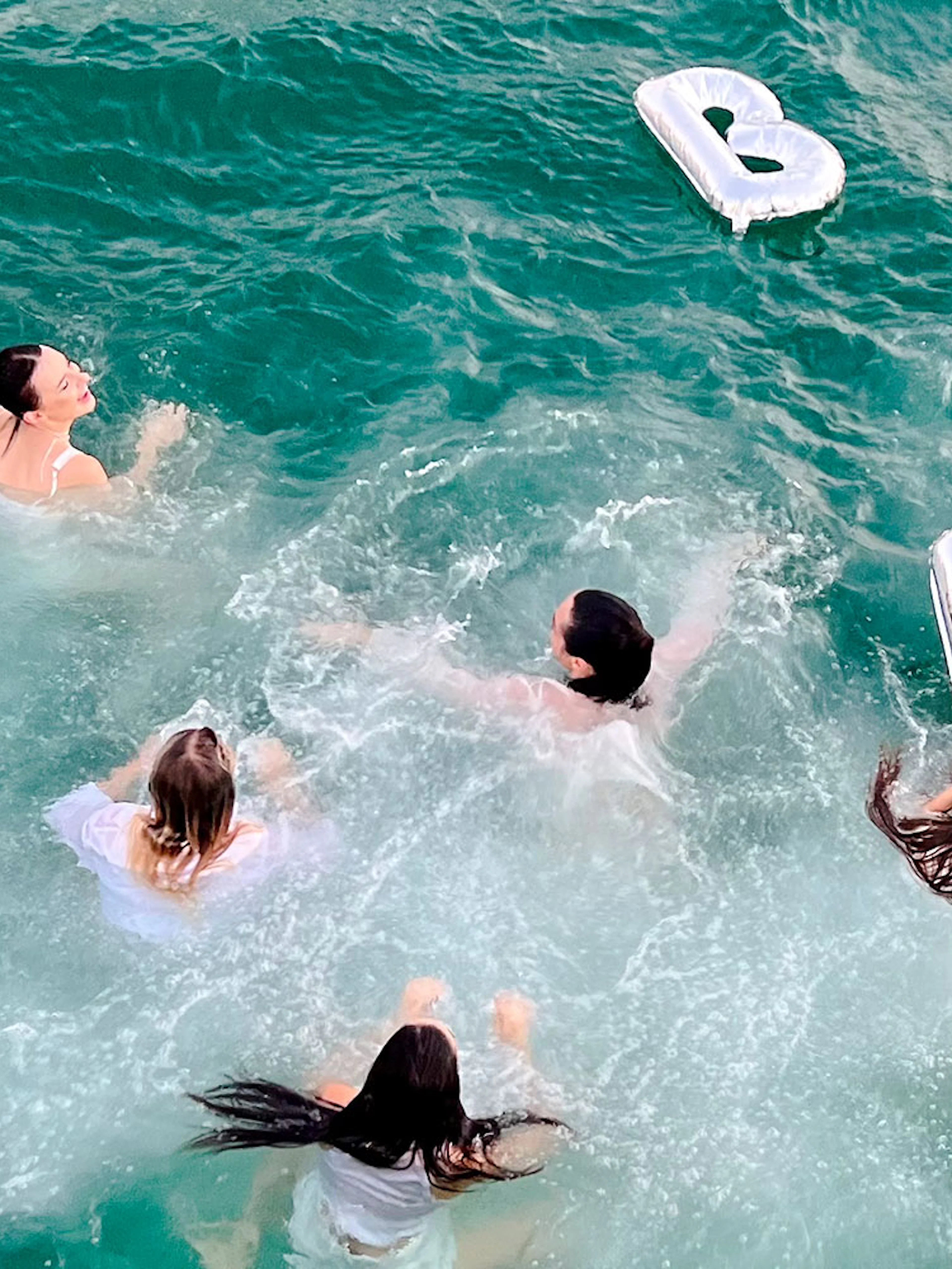 Tourists swimming with inflatable letters in the sea during a luxury yacht tour in Dubai.