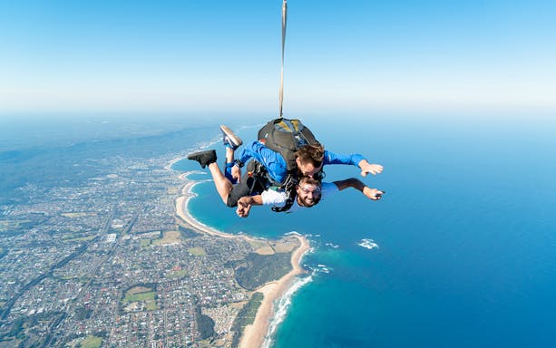 Tandem skydiving over Wollongong, Sydney, with instructor and participant in freefall above coastline.