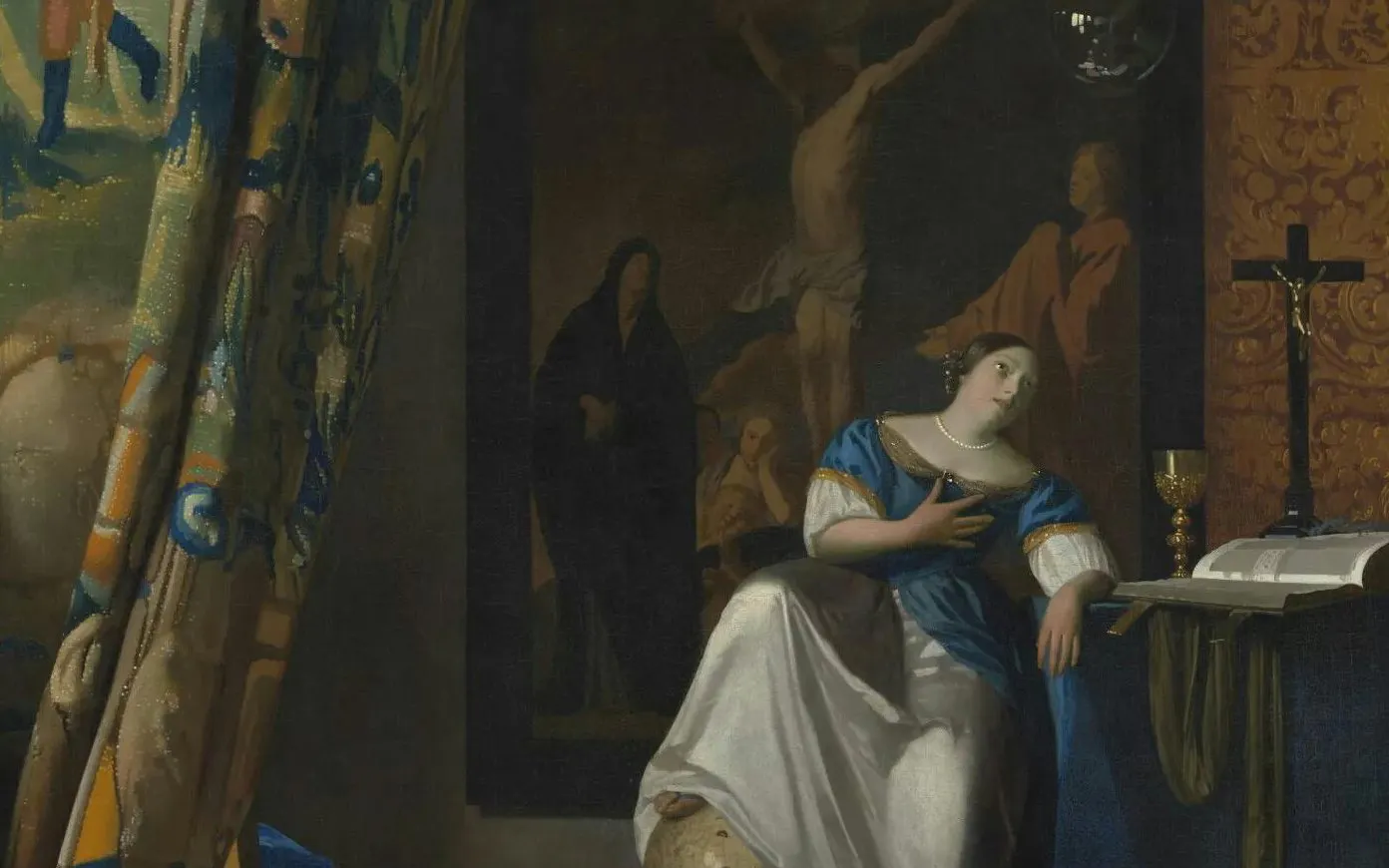 Woman in blue dress seated by a table with a book and chalice at Fabrique des Lumières.