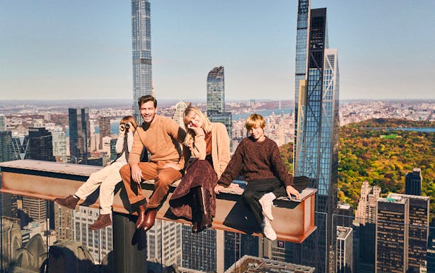 Family sitting on a beam with New York skyline view from Top of the Rock.