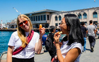Tourists enjoying simit by the waterfront in Istanbul during a food tour.