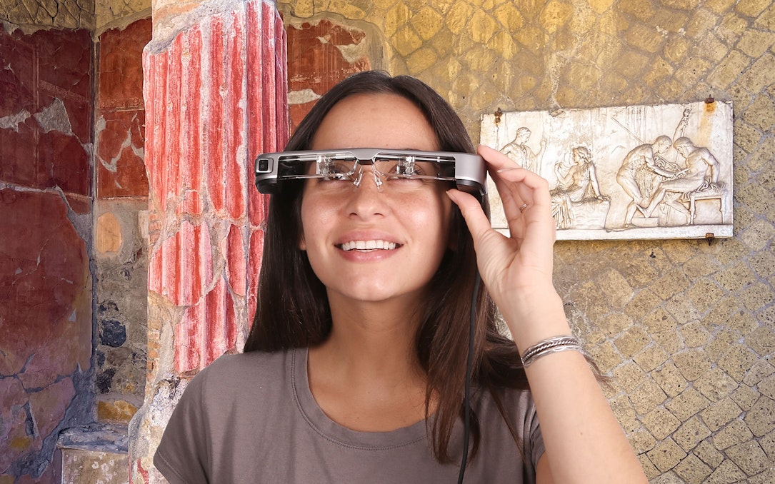 Person using augmented reality glasses at Herculaneum ruins with ancient frescoes.