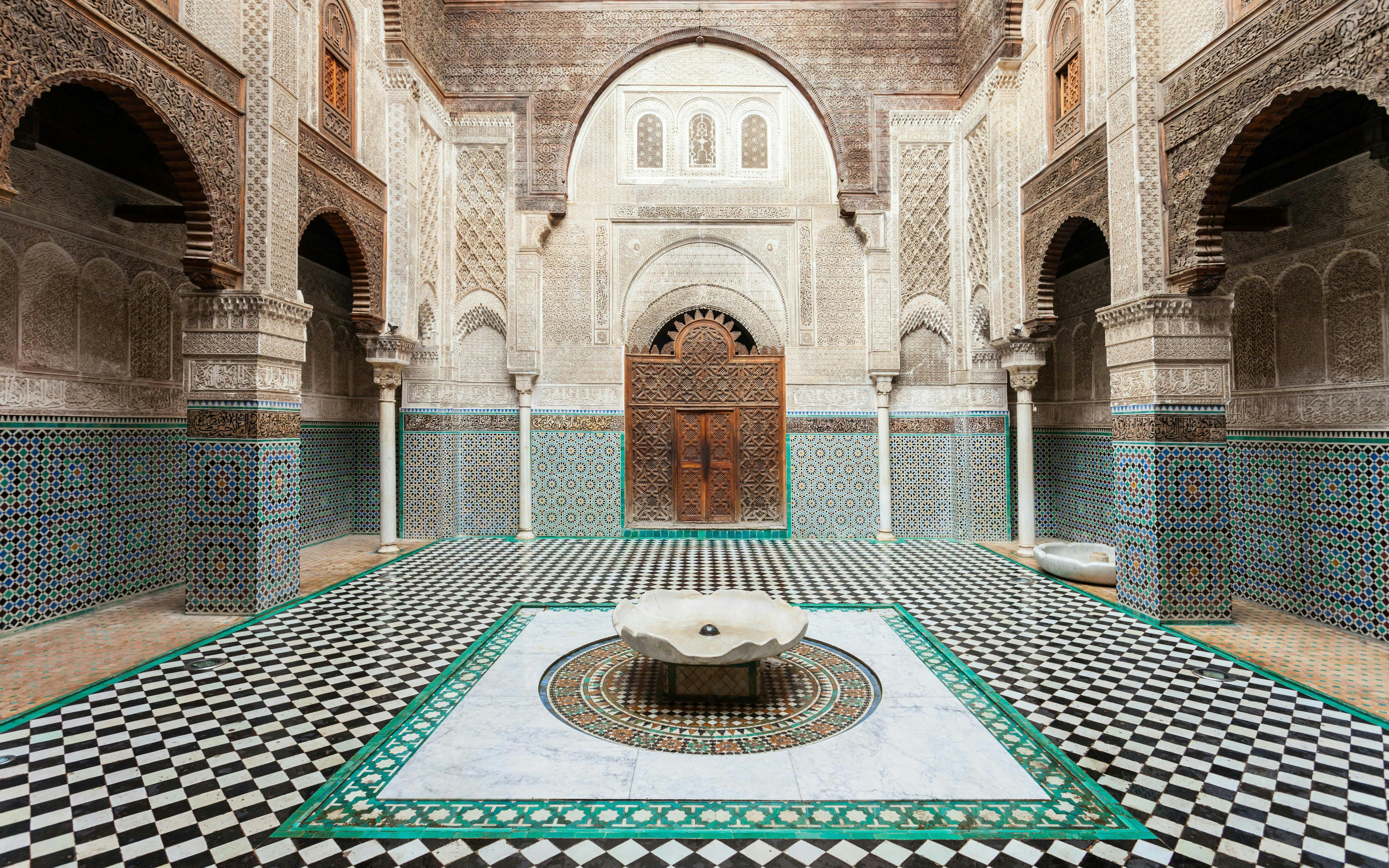 Al Attarine Madrasa courtyard with intricate tilework and carved wooden door in Fez, Morocco.