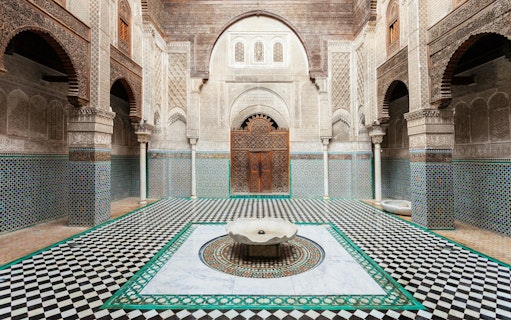 Al Attarine Madrasa courtyard with intricate tilework and carved wooden door in Fez, Morocco.