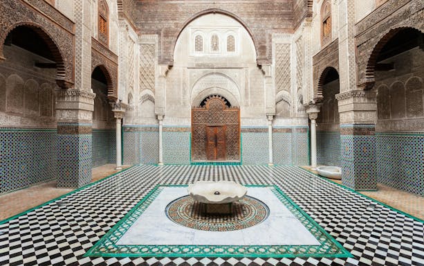 Al Attarine Madrasa courtyard with intricate tilework and carved wooden door in Fez, Morocco.