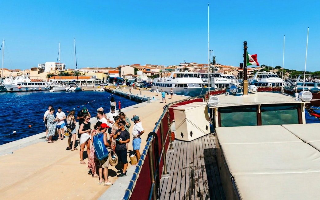 Tourists boarding a motorboat for a La Maddalena Archipelago tour, docked at a vibrant marina.