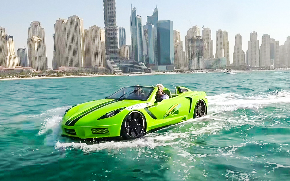 Man driving a green jet car corvette on water with Dubai skyline in the background.