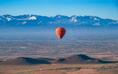 Hot air balloon over desert near Marrakech with Atlas Mountains in background.