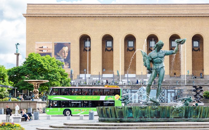 Götaplatsen square with hop-on hop-off bus, Gothenburg, featuring Poseidon statue and city architecture.
