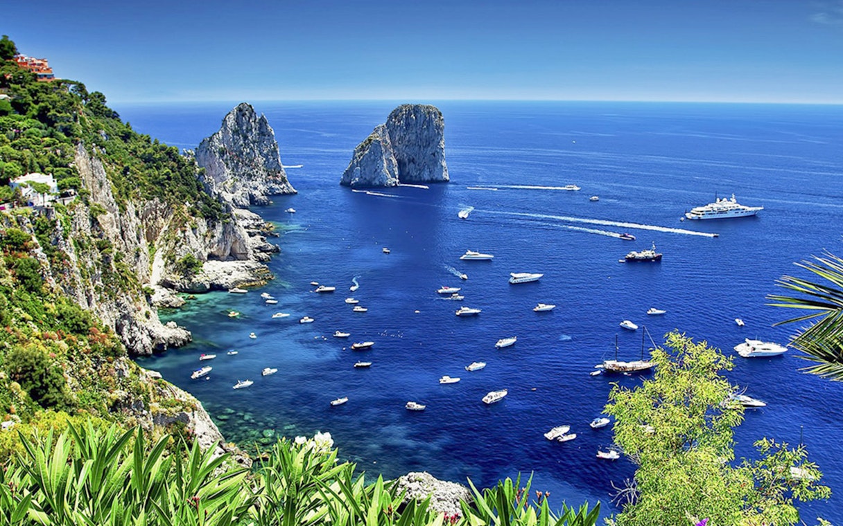 Boats in the blue waters near Faraglioni rocks, Capri Island, Italy.