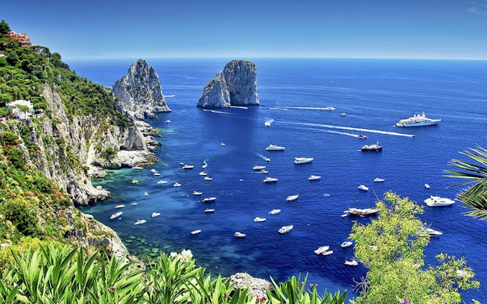 Boats in the blue waters near Faraglioni rocks, Capri Island, Italy.