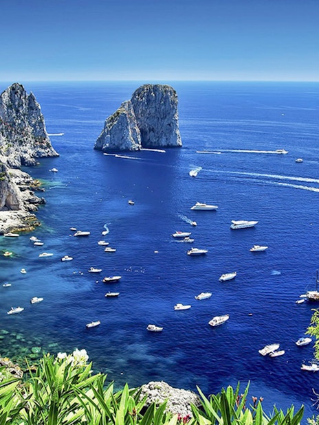 Boats in the blue waters near Faraglioni rocks, Capri Island, Italy.