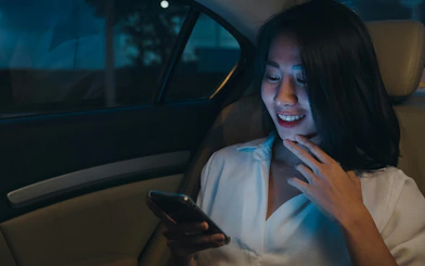 Woman using smartphone in backseat of car at night.