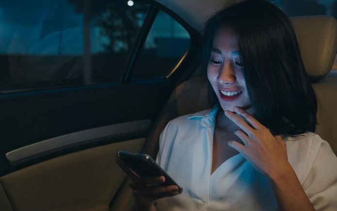Woman using smartphone in backseat of car at night.