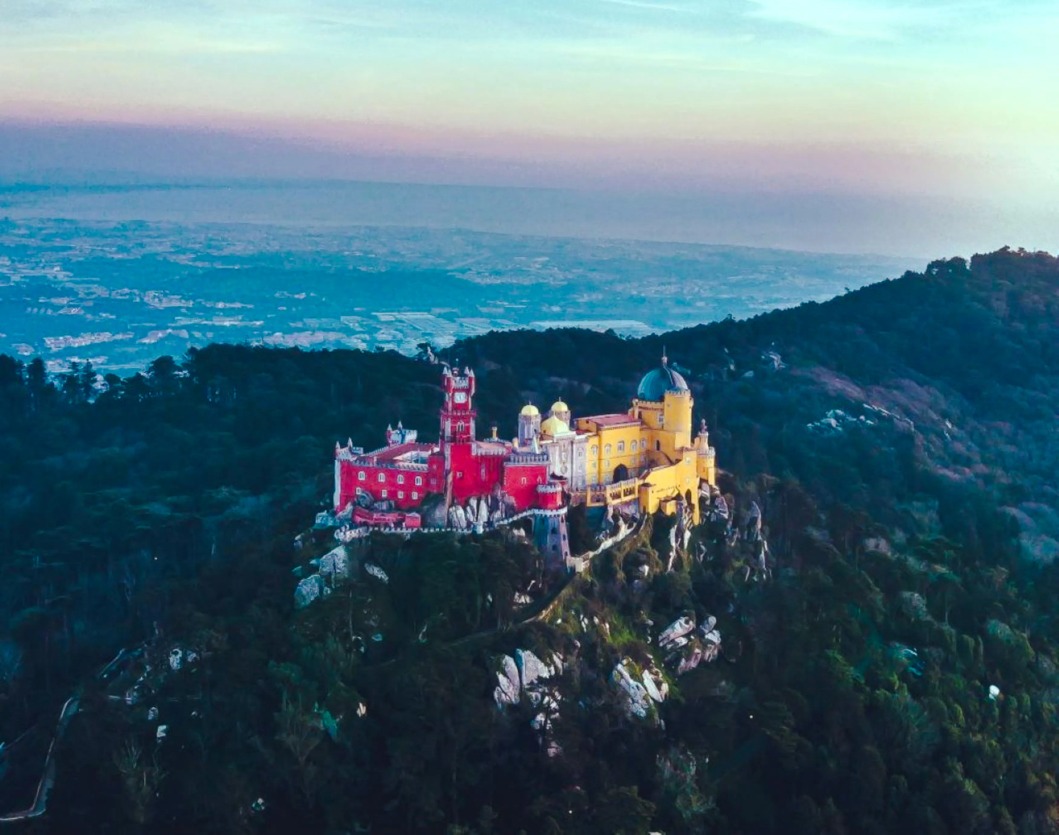 Aerial view of Palácio Nacional da Pena in Sintra, colorful palace on a hilltop surrounded by forest.