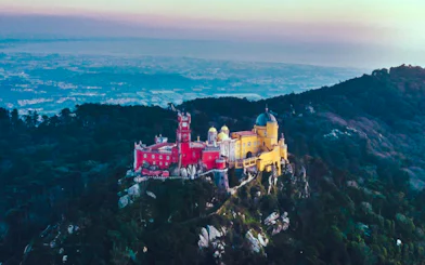 Aerial view of Palácio Nacional da Pena in Sintra, colorful palace on a hilltop surrounded by forest.