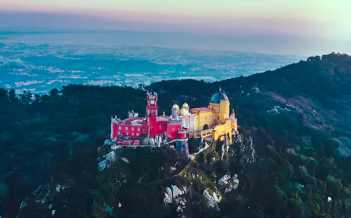 Aerial view of Palácio Nacional da Pena in Sintra, colorful palace on a hilltop surrounded by forest.
