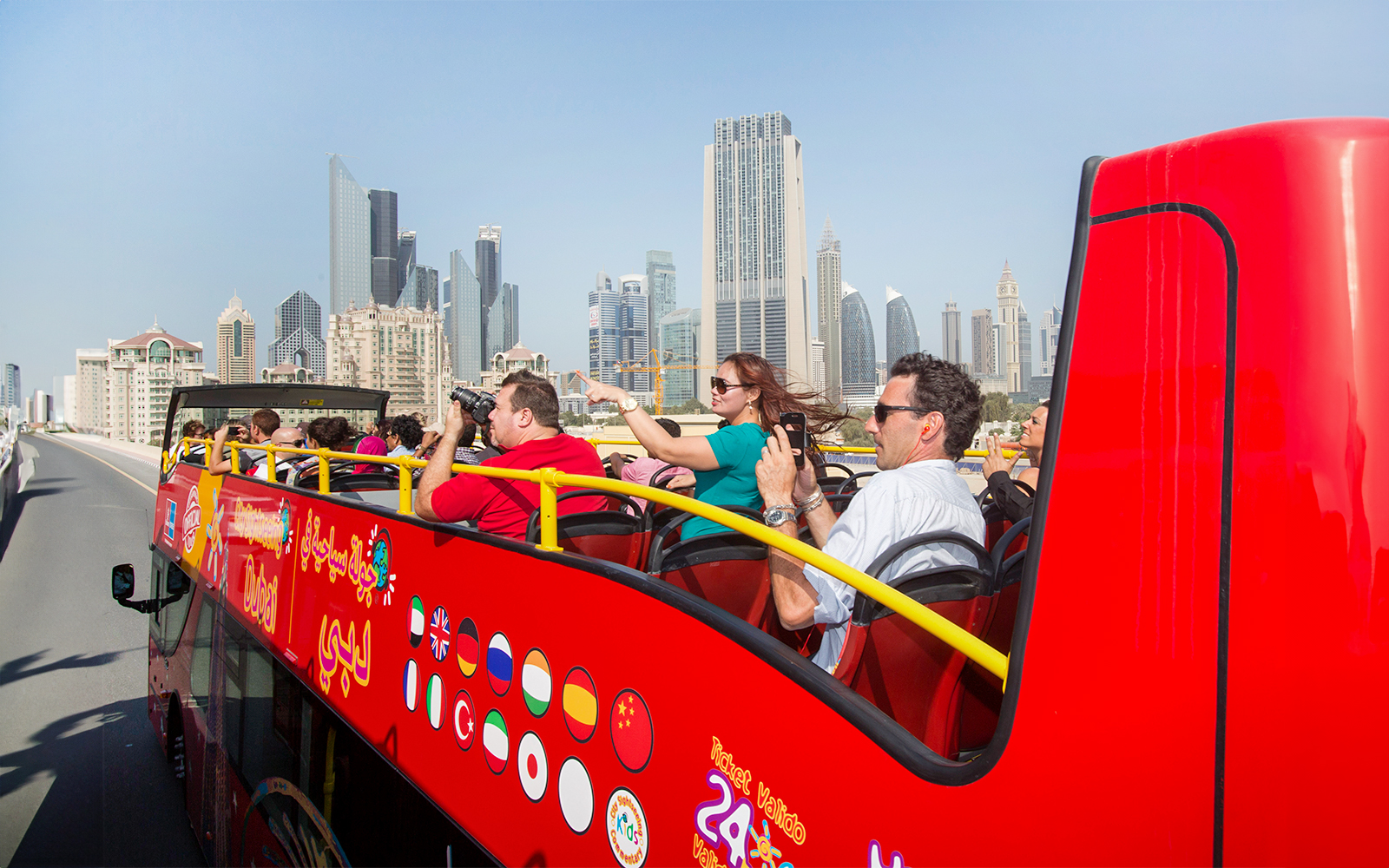 Tourists on a red Citysightseeing bus in Dubai with skyscrapers in the background.