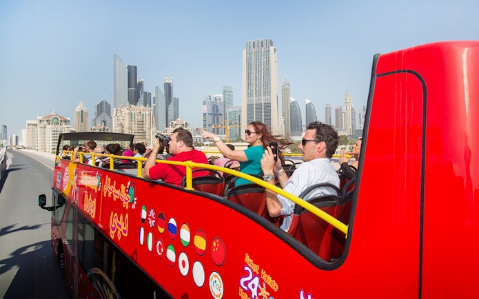 Tourists on a red Citysightseeing bus in Dubai with skyscrapers in the background.