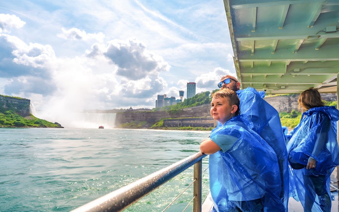 Family on a boat tour at Niagara Falls, wearing blue ponchos, with mist and skyline in view.