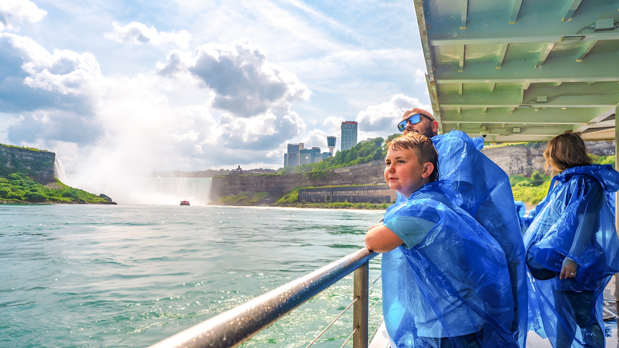 Family on a boat tour at Niagara Falls, wearing blue ponchos, with mist and skyline in view.