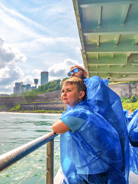 Family on a boat tour at Niagara Falls, wearing blue ponchos, with mist and skyline in view.